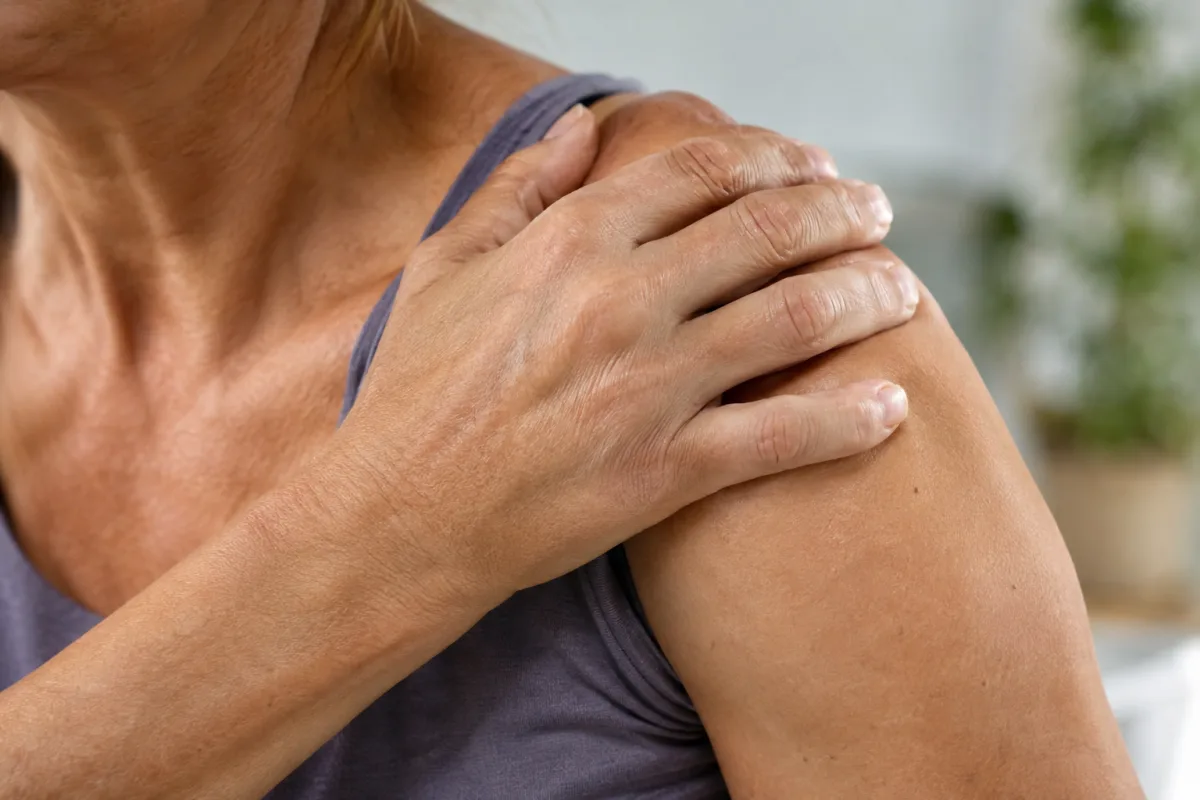 Gros plan sur les mains bienveillantes d'un soignant appliquant une compresse chaude sur une épaule